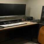 A home recording setup with microphone, laptop audio waveforms, and audio gear for ai voiceover jobs.