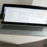 A minimalist home office desk setup with a laptop displaying document forms for digital account registration.