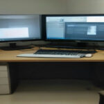 A modern laptop, headphones, and foot pedal sitting on an organized desk for home-based audio transcription.