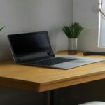 A modern minimalist desk with a laptop and credit card on a wooden surface in daylight.