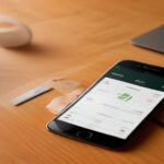 A smartphone and debit card resting on a wooden desk illustrating digital money management security.