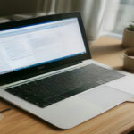 Remote worker reviewing online contractor guidelines and task portals on a laptop at a clean daylight workspace.