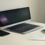 A smartphone displaying a mobile game resting on a modern clean wooden desk beside a notebook.